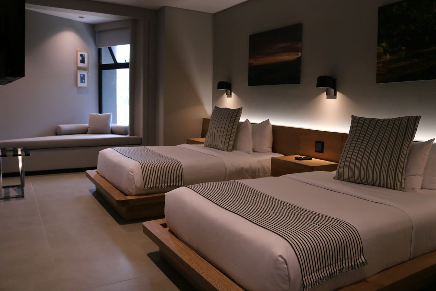 Habitación de hotel moderna con dos camas y un banco junto a la ventana.