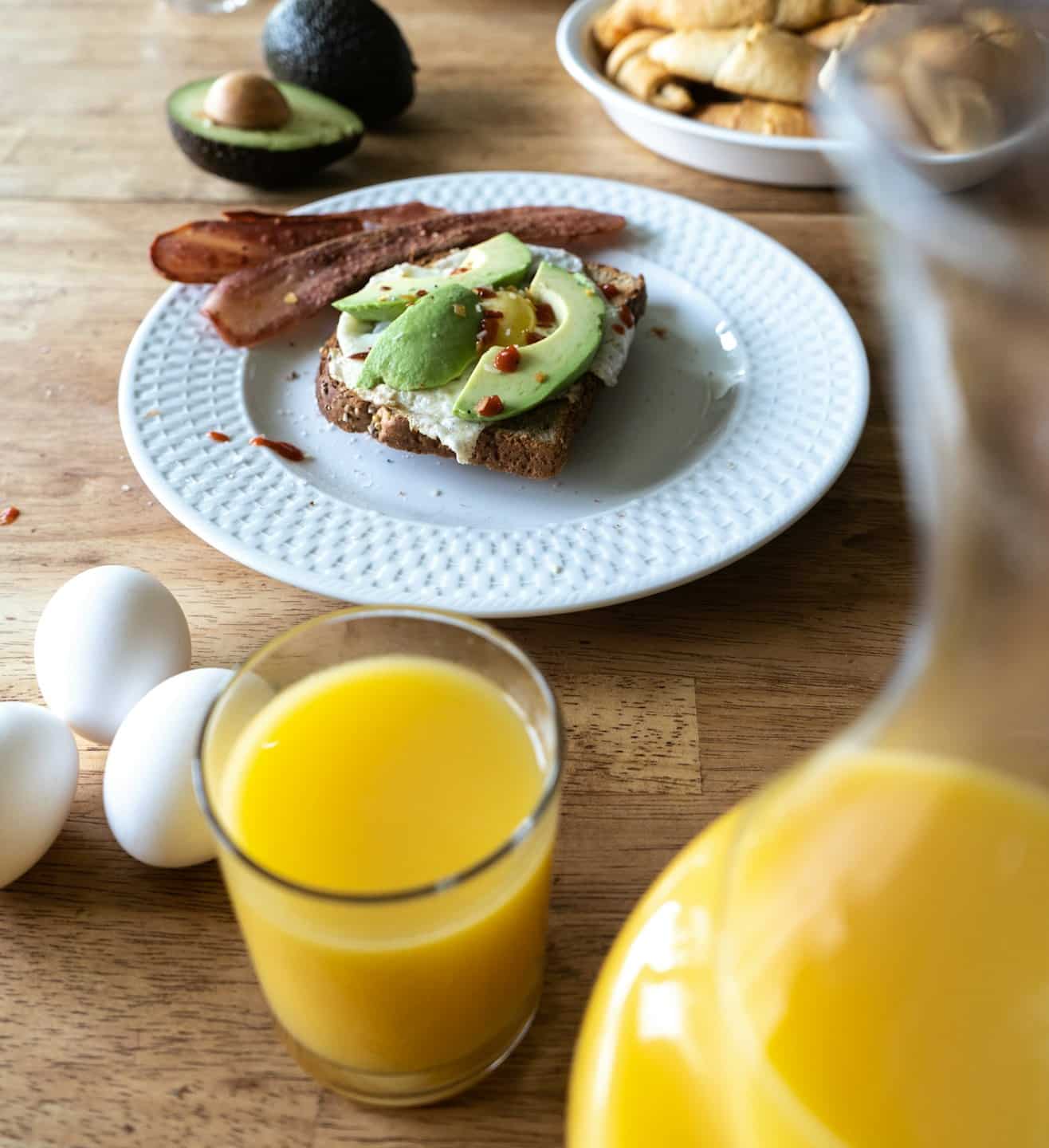 Tostada de aguacate con huevo frito y tocino sobre una mesa de madera.