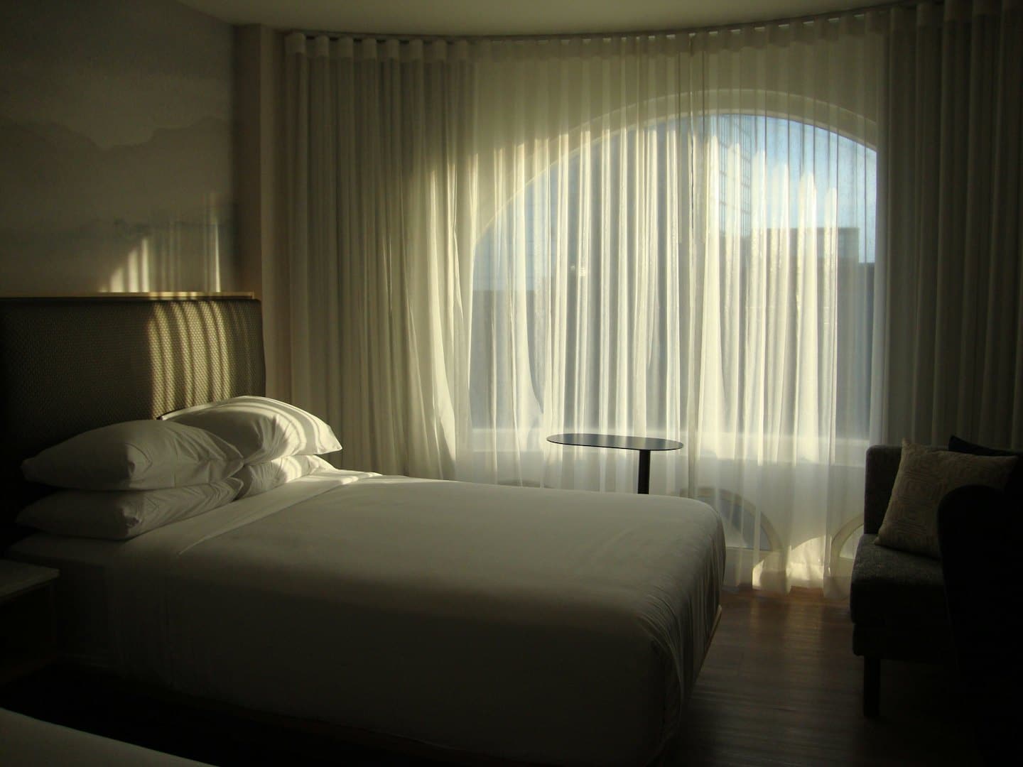 Habitación de hotel minimalista con cama bien hecha y ventana arqueada.