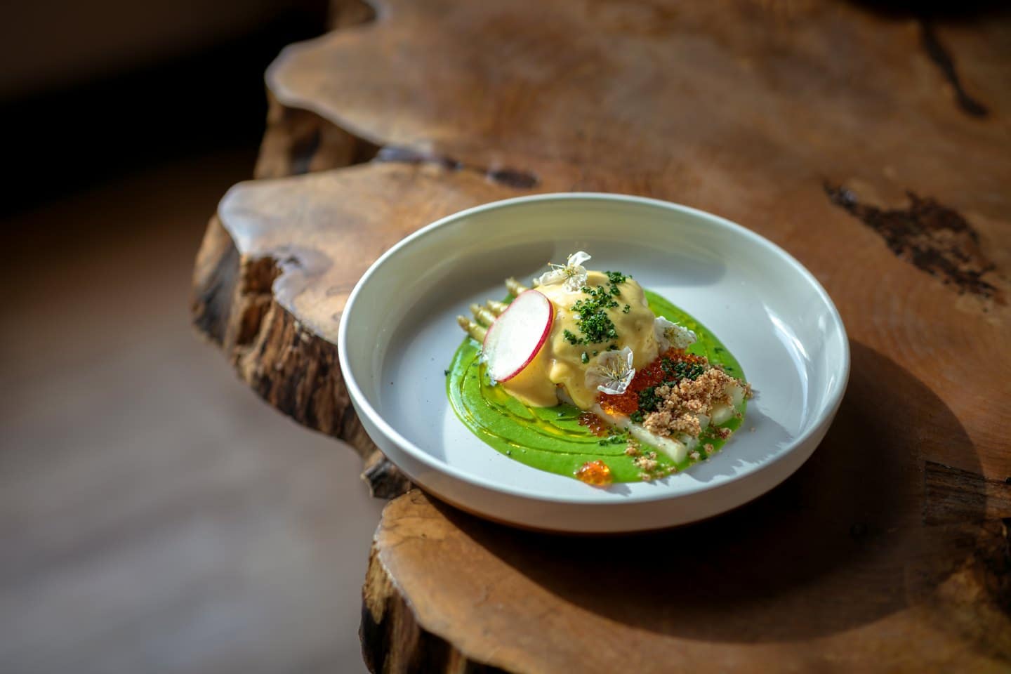 Plato gourmet con salsa colorida, huevas y flores sobre mesa de madera.
